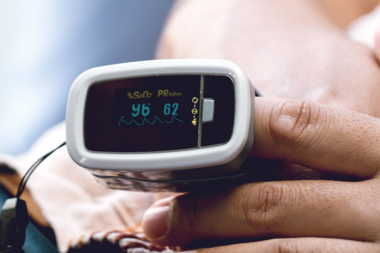 A person is wearing a pulse oximeter on their finger to monitor pulse rate and blood oxygen levels