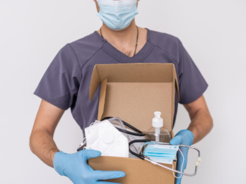 A man carrying a box of medical supplies while wearing gloves and a surgical mask.