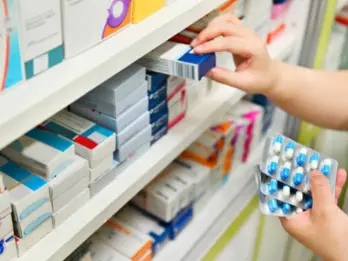 A person is taking a package of tablets for a prescription from the pharmacy shelf.